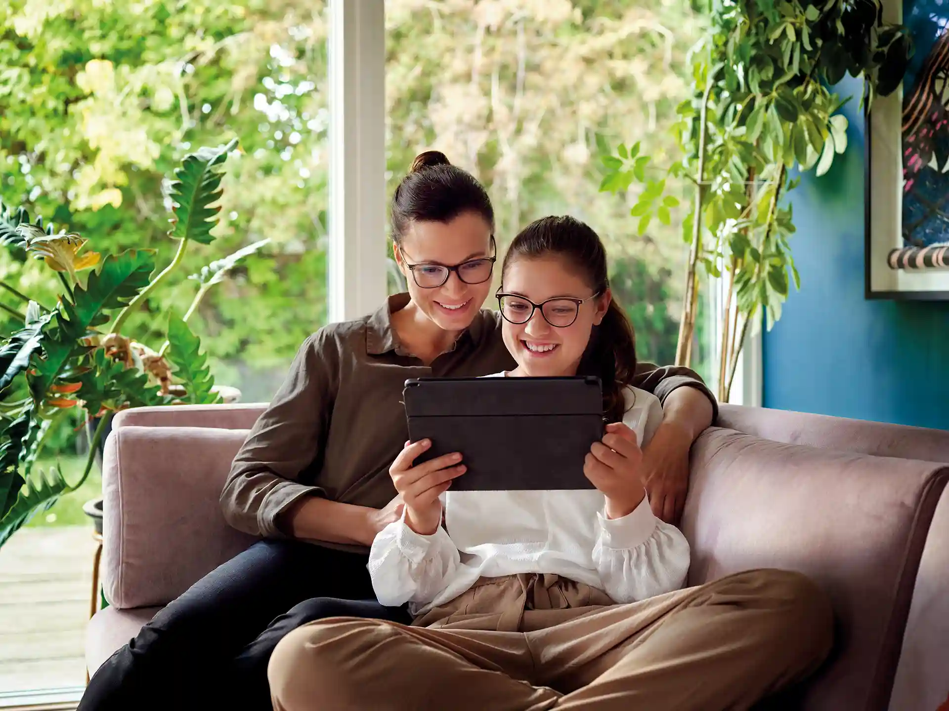 Frau mit Tochter sintzen auf einem Sofa und schauen gemeinsam auf ein Tablet